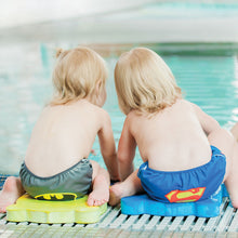 Boy in batman swim diaper and boy in superman swim diaper sitting by the pool